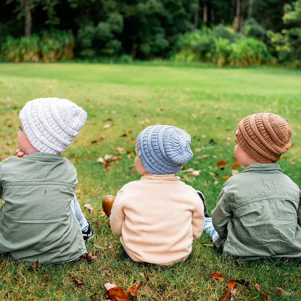 Three children wearing Byron Beanies in Speckle, Slate and Mocha while sitting outdoors