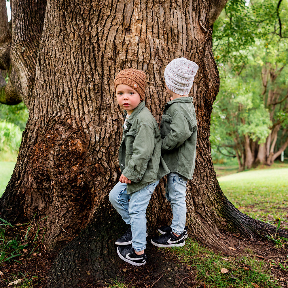 Two children wearing Mocha and Speckle Byron Beanies together beside a tree