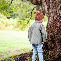 Back view of a child wearing the Mocha Byron Beanie beside a tree