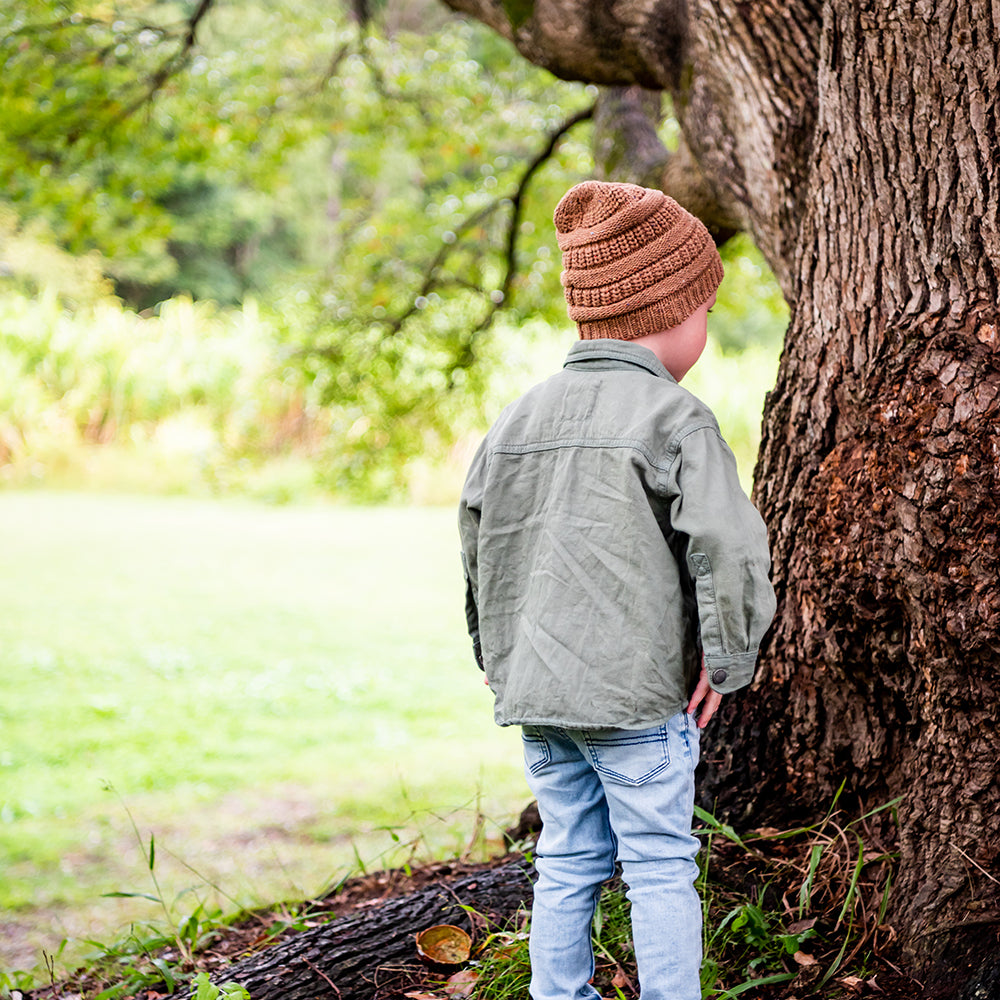 Back view of a child wearing the Mocha Byron Beanie beside a tree