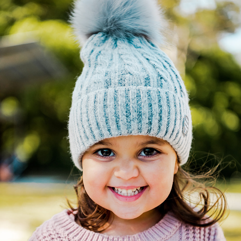 Girl wearing the Grey Aurora Beanie outdoors, showing the cable knit and fluffy pom-pom