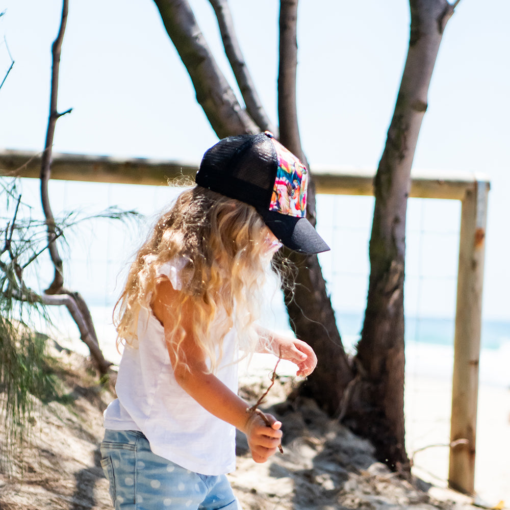 Child walking at the beach wearing the Flock Trucker Cap, showing its colourful front and black mesh back