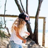 Child walking at the beach wearing the Flock Trucker Cap, showing its colourful front and breathable black mesh back