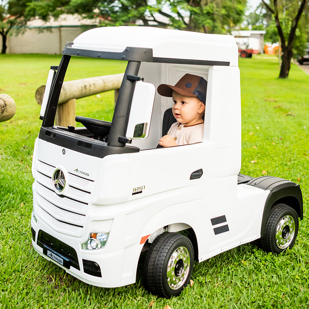 Toddler wearing the Chocolate Trucker Cap while riding in a white toy truck outdoors