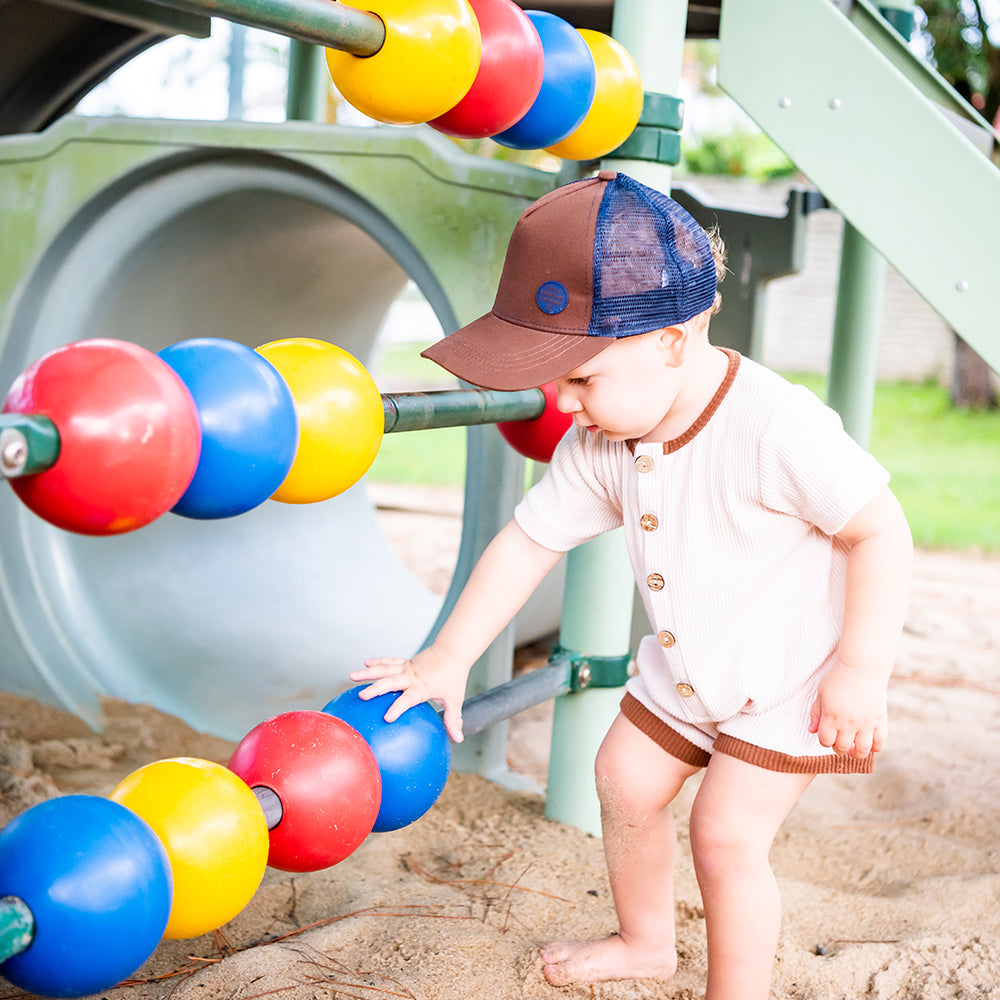Toddler wearing the Chocolate Trucker Cap while playing with colourful playground equipment
