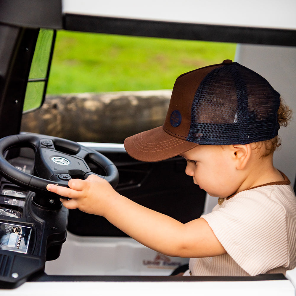 Toddler wearing the Chocolate Trucker Cap while driving a toy truck, showing the cap’s side profile and breathable navy mesh