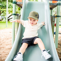 Child wearing the Hunter Trucker Cap while playing on a playground slide