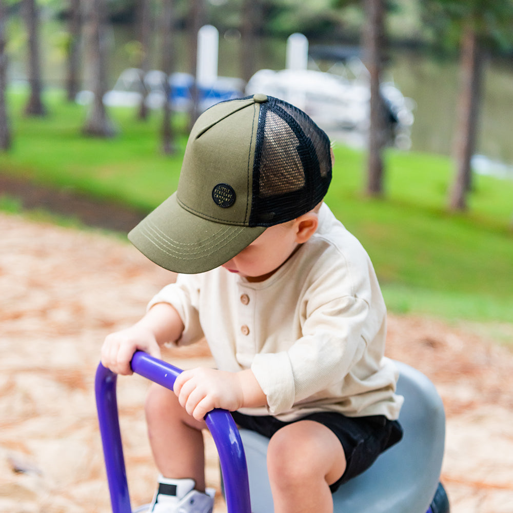 Child wearing the forest green Hunter Trucker Cap at the playground showing the curved peak and black mesh side