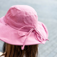 Close-up of the Musk Sun Hat showing the pink linen texture, wide brim and circumference strap tied in a bow