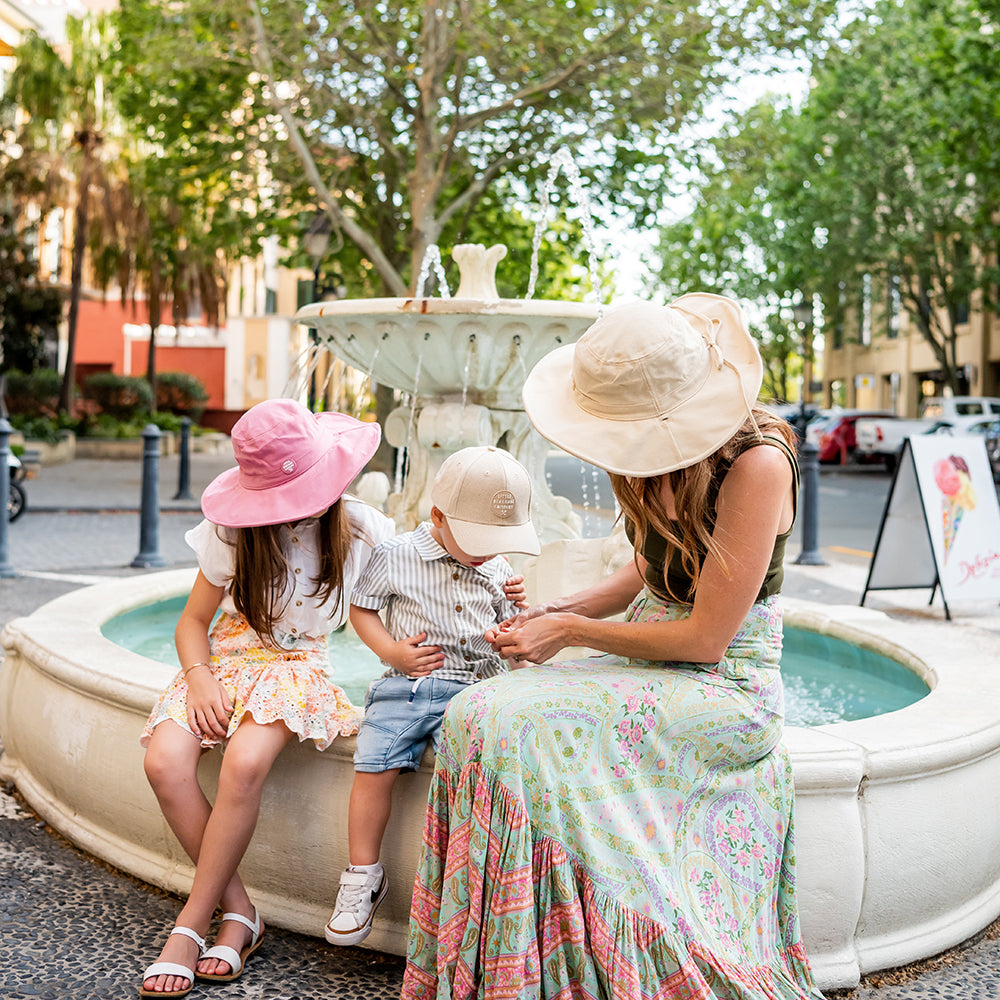 Adult wearing the Oatmeal Sun Hat with children during a family outing by a fountain