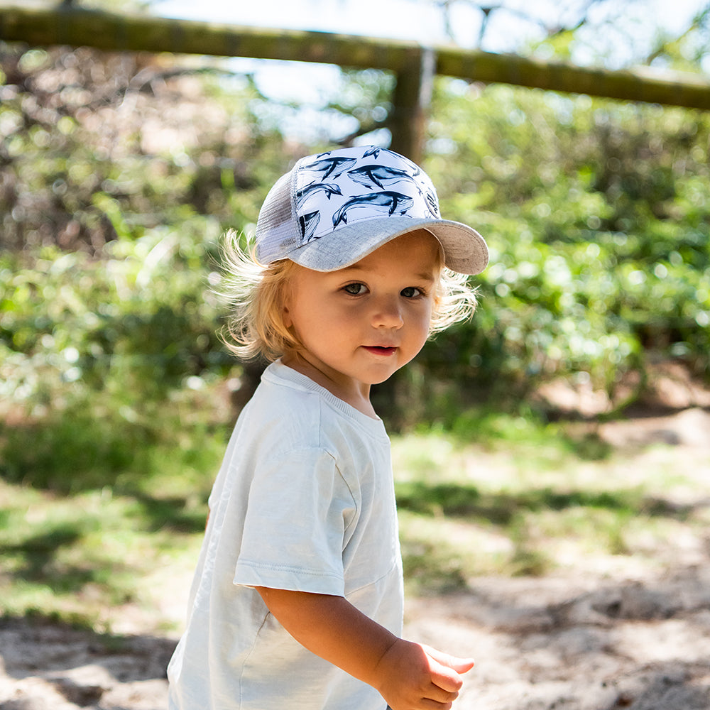 Child wearing the Pod Trucker Cap outdoors showing its watercolour whale print and grey curved peak