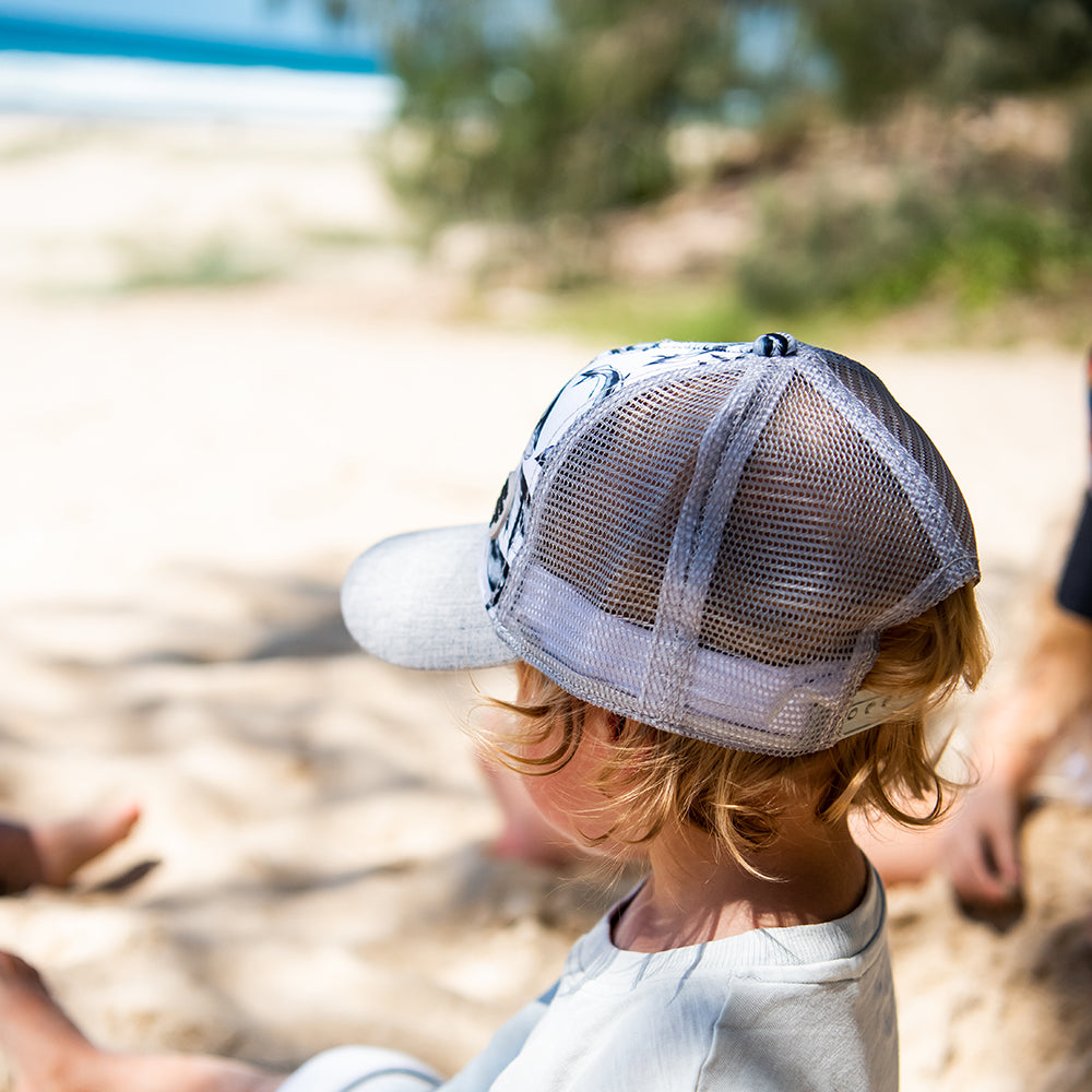 Close-up of a child wearing the Pod Trucker Cap showing the whale print, grey peak and breathable mesh