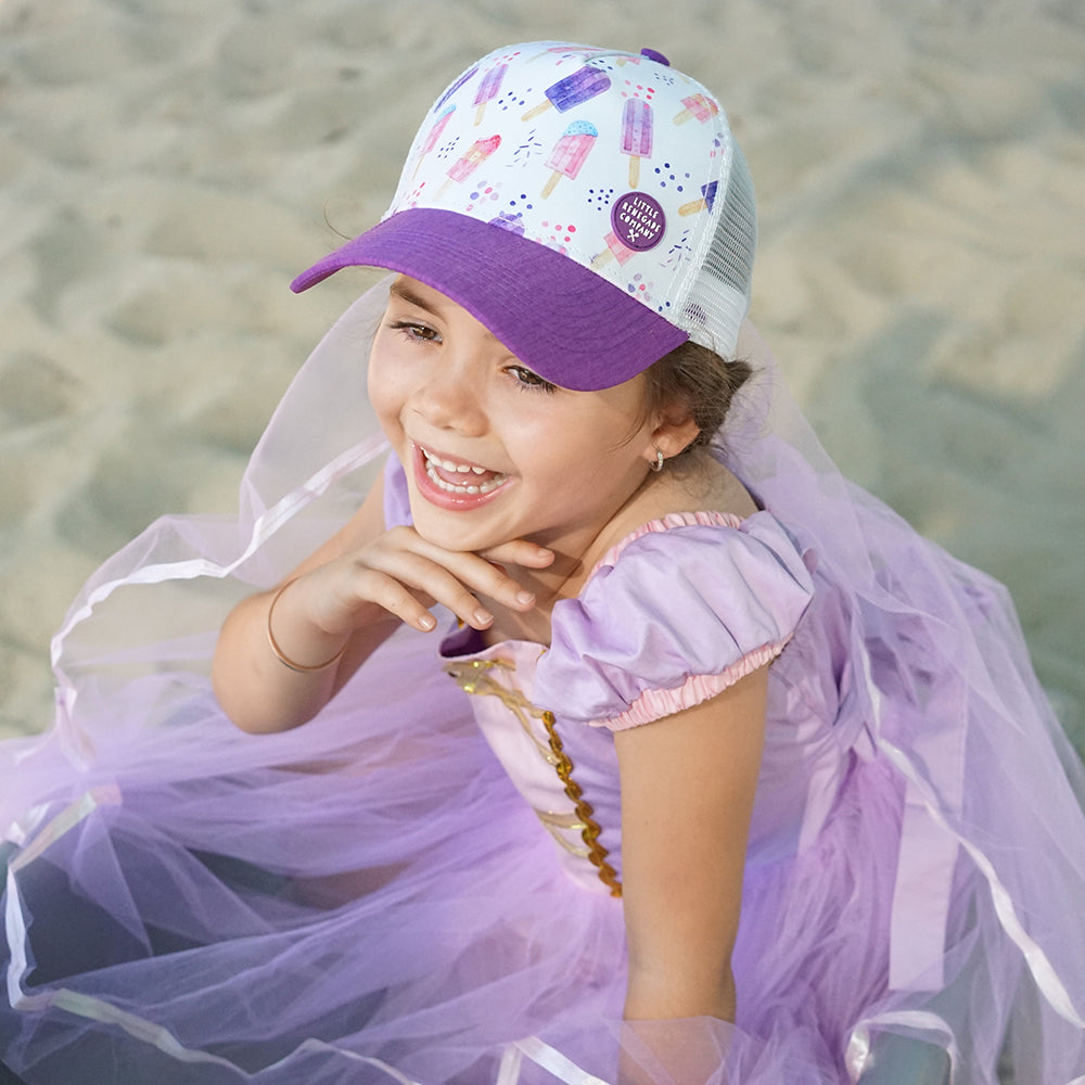 Child wearing the Popsicle Trucker Cap outdoors showing its colourful popsicle print, purple curved peak and white mesh