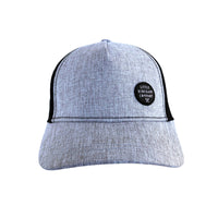 Young child wearing the Shadow Trucker Cap outdoors on grass, showing its textured grey front and black mesh side