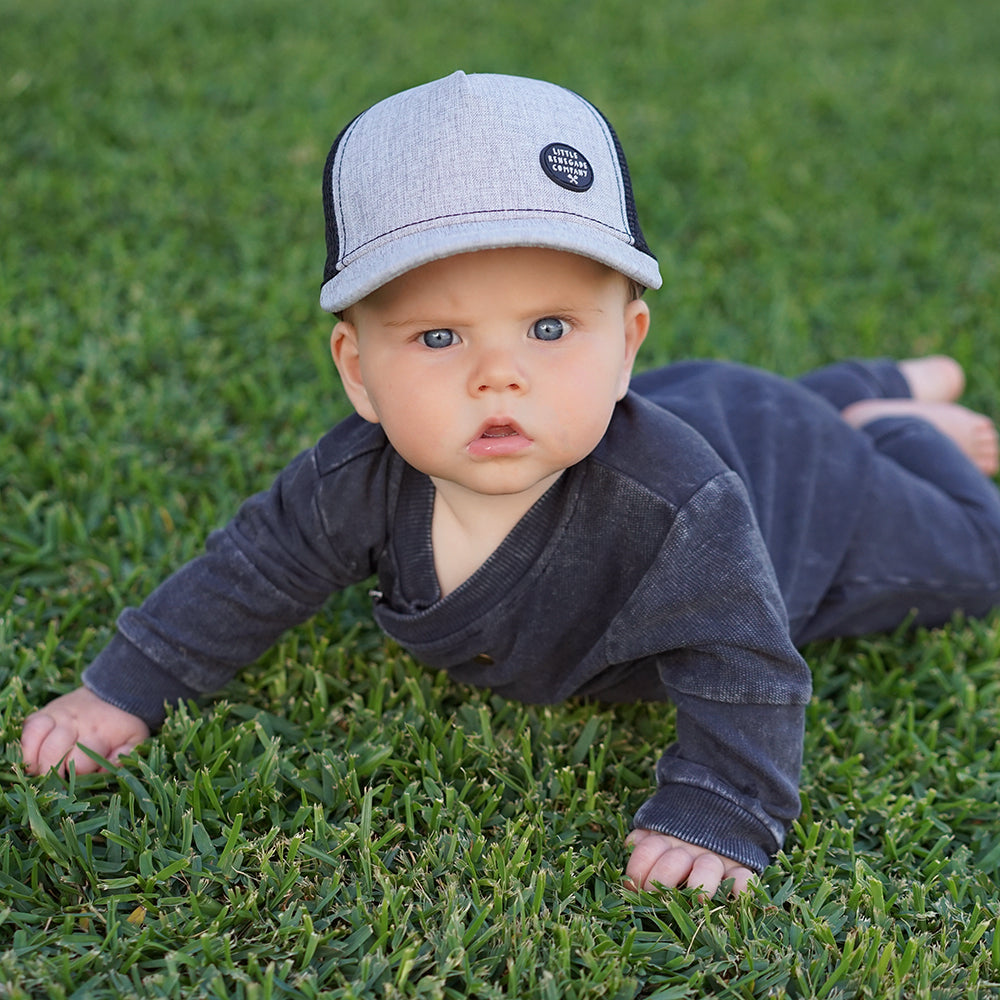 Young child wearing the Shadow Trucker Cap outdoors on grass, showing its textured grey front and black mesh side