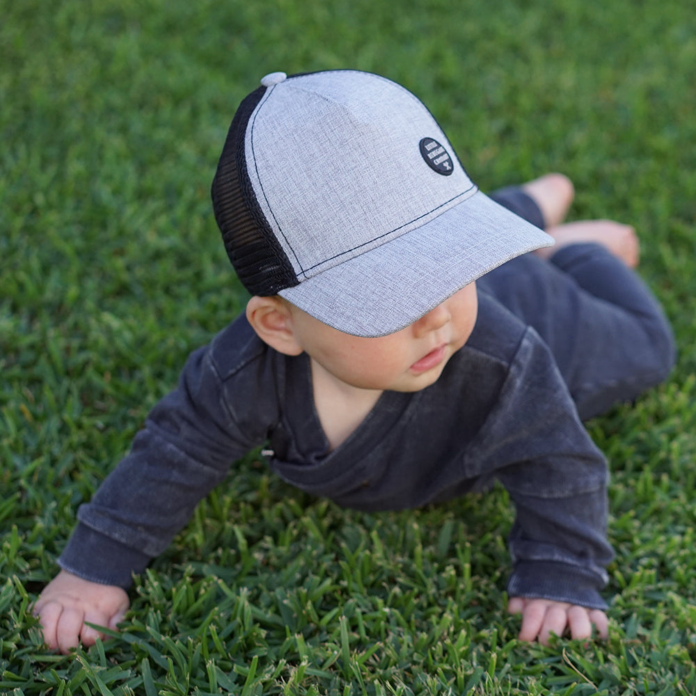 Close-up of a child wearing the Shadow Trucker Cap showing its textured grey front, curved peak and black mesh
