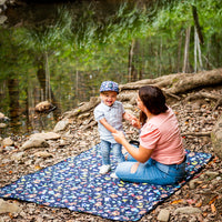 Parent and child sitting together on the Superhero Pals Adventure Mat outdoors