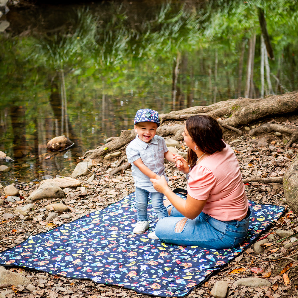 Parent and child sitting together on the Superhero Pals Adventure Mat outdoors