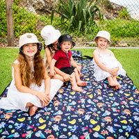 Family and friends sitting together on the Superhero Pals Adventure Mat outdoors