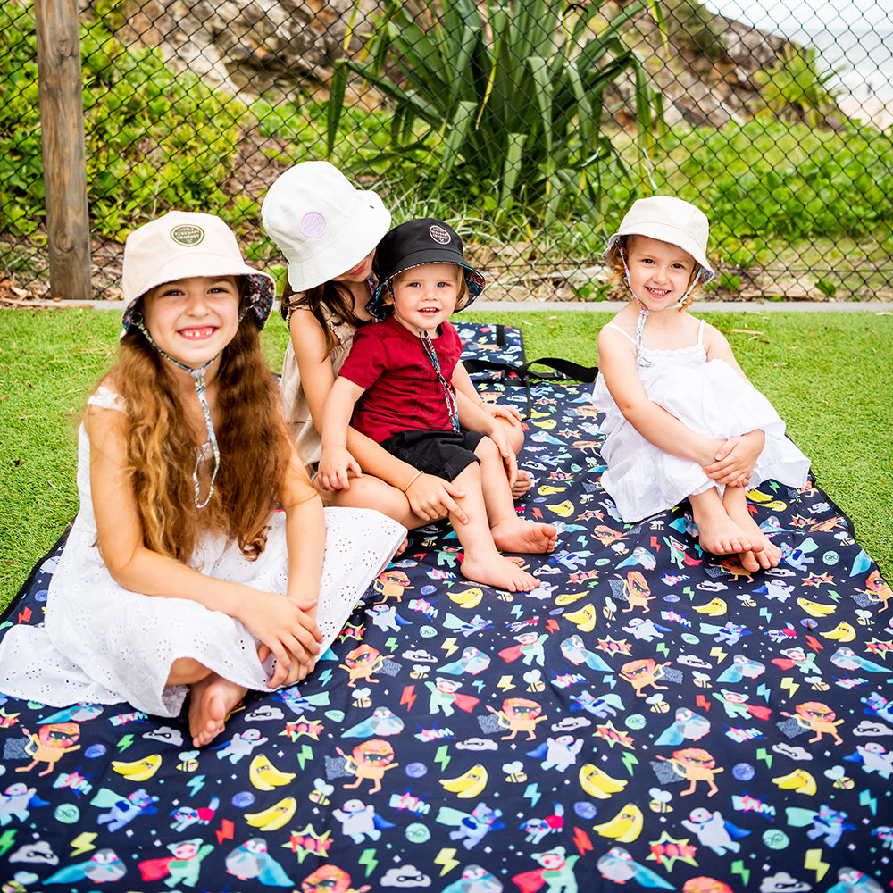 Family and friends sitting together on the Superhero Pals Adventure Mat outdoors