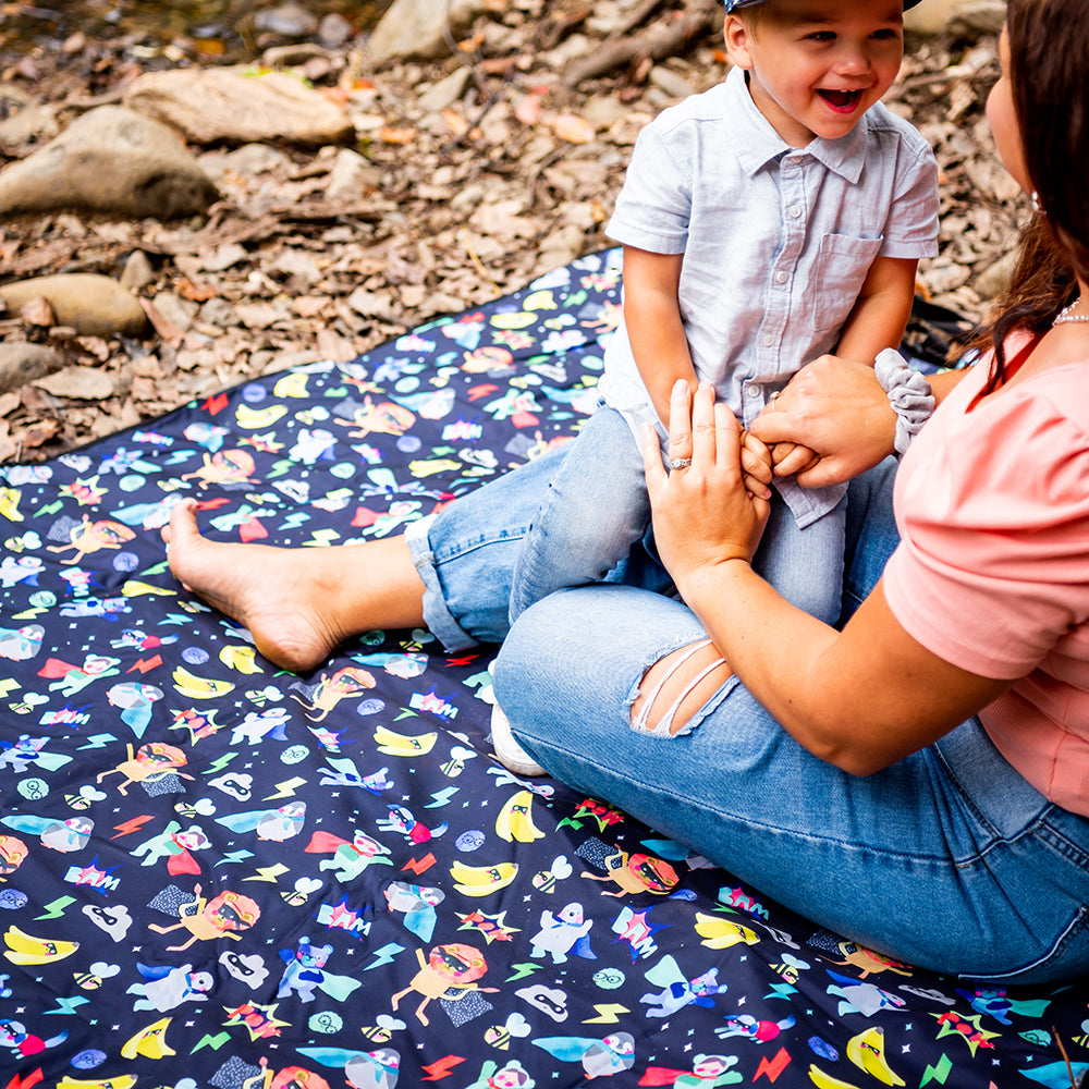 Child sitting on the Superhero Pals Adventure Mat outdoors showing its colourful superhero print