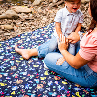 Child sitting on the Superhero Pals Adventure Mat outdoors showing its colourful superhero print