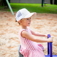 Child wearing the Wheat Trucker Cap outdoors showing its soft neutral front, curved peak and white mesh